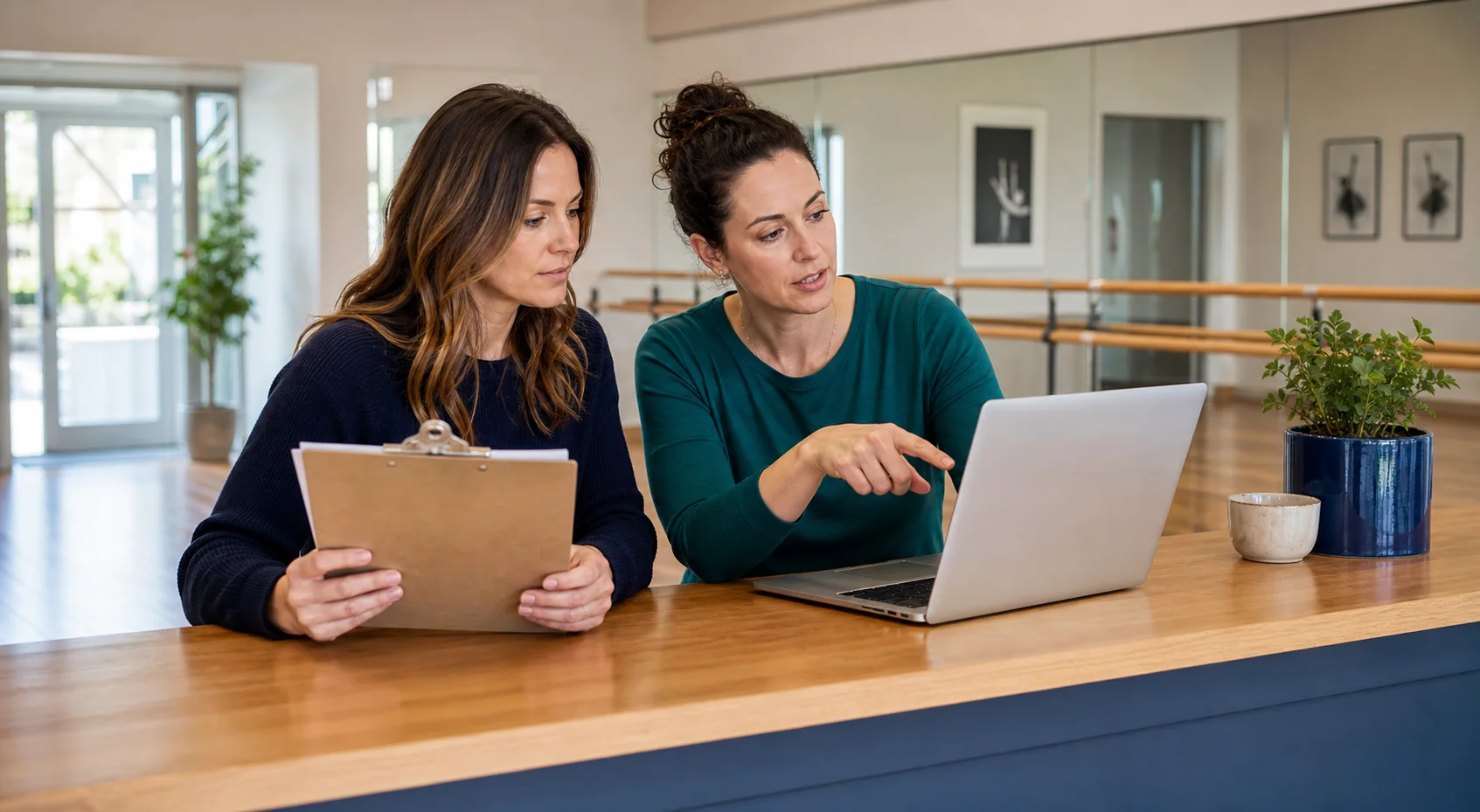 Two women at a studio front desk working through the schedule together on a laptop